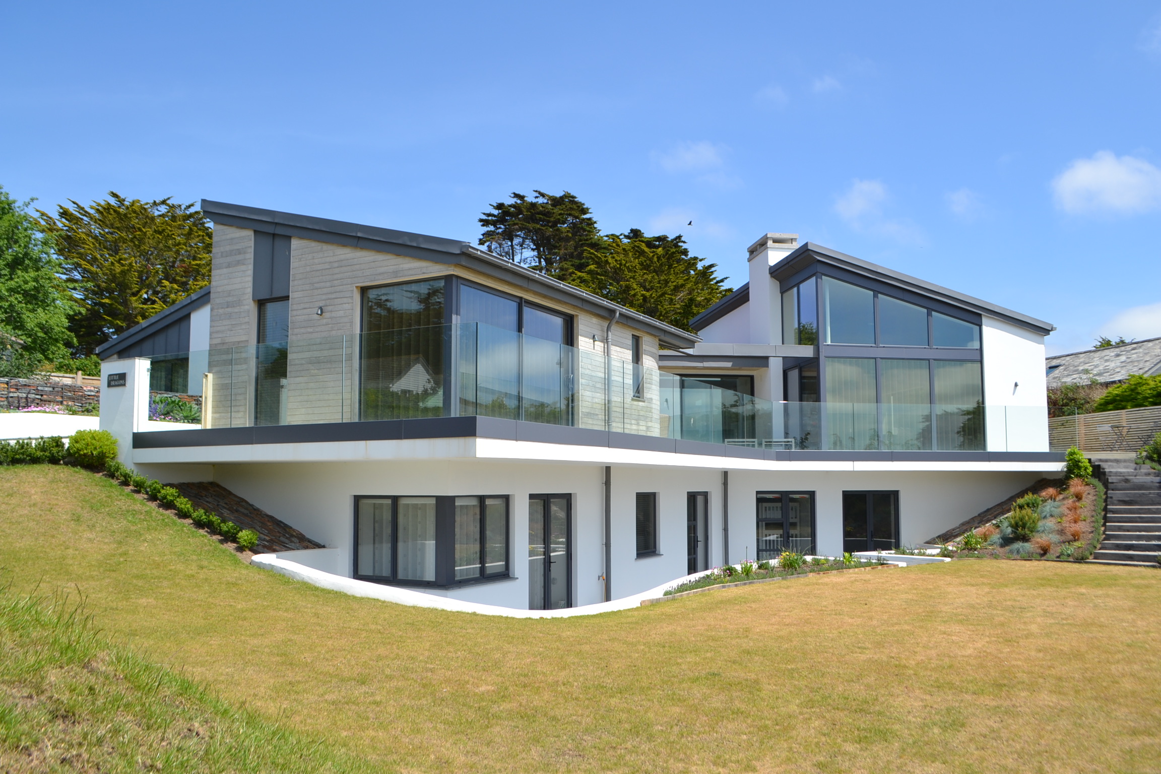 House exterior, cantilevered deck, landscaped garden, floor to ceiling glazing in steel frame first floor.