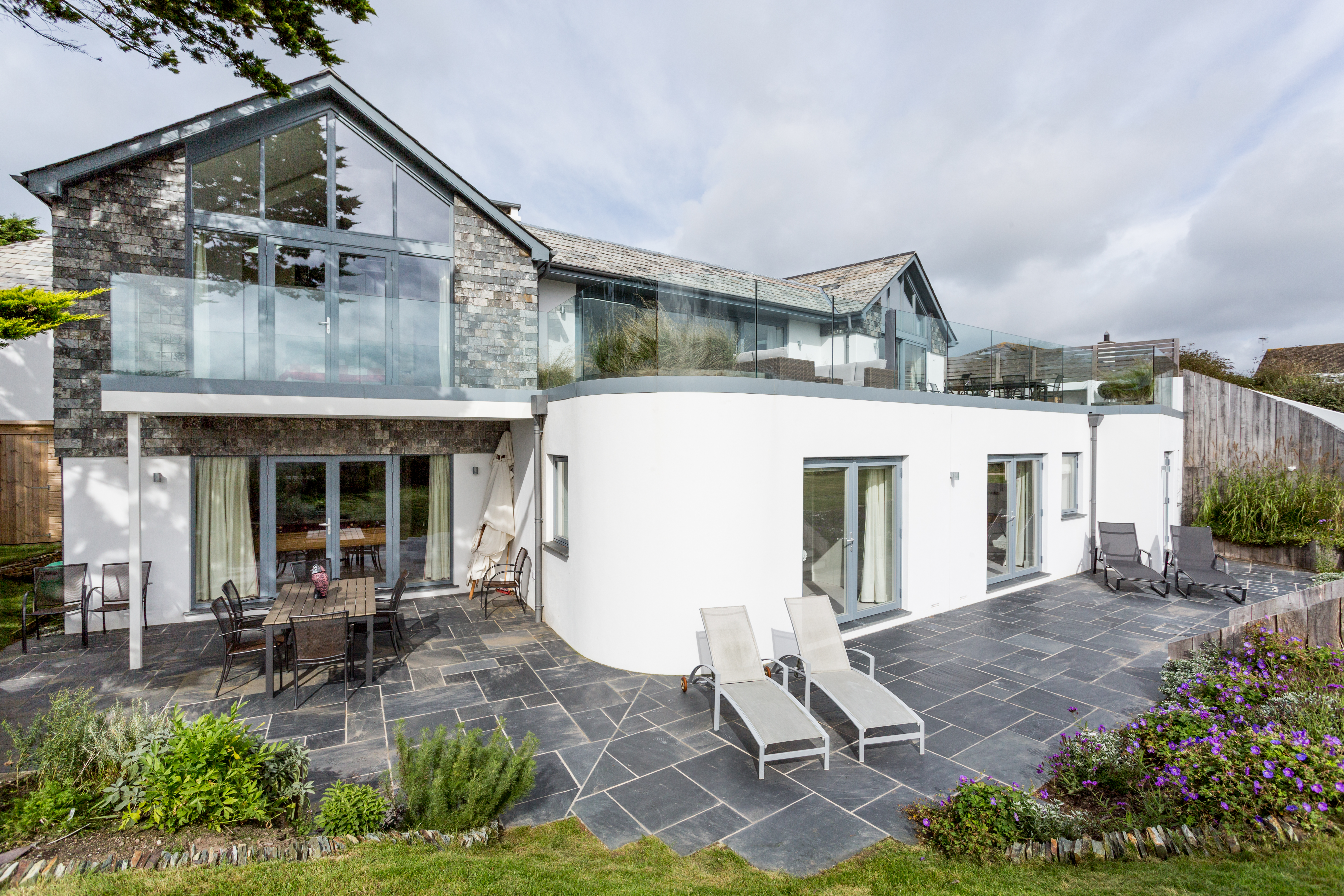 Ground floor slate patio, showing engineered curved wall to bedroom, curved frameless glass balustrade