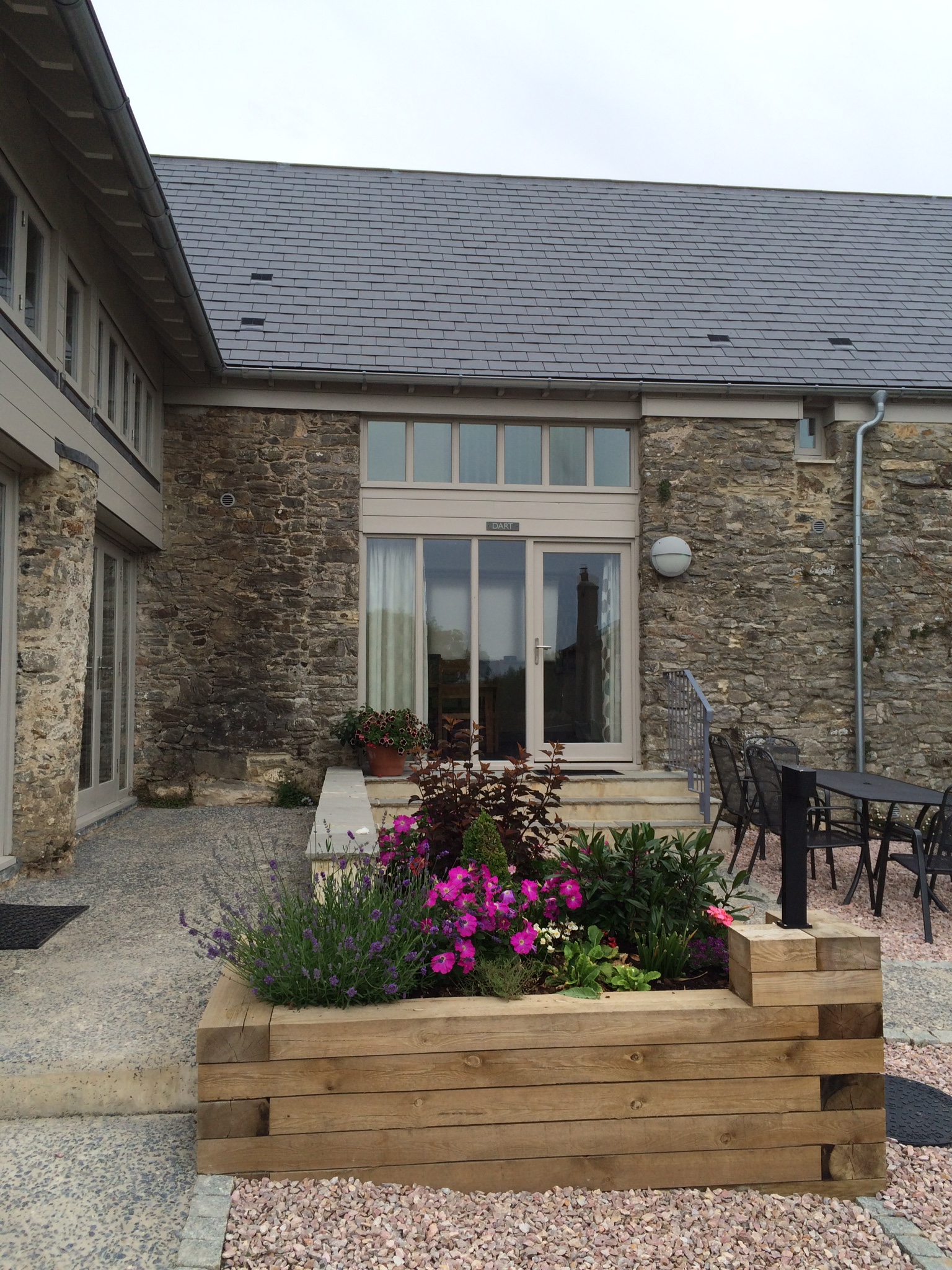 Barn conversion, new slate roof, repointed walls, timber planter with flowers in foreground.